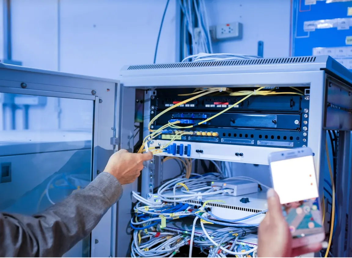 Technician organizing Ethernet and fiber cables inside a network rack, illustrating structured cabling systems and color-based cable identification in commercial network environments